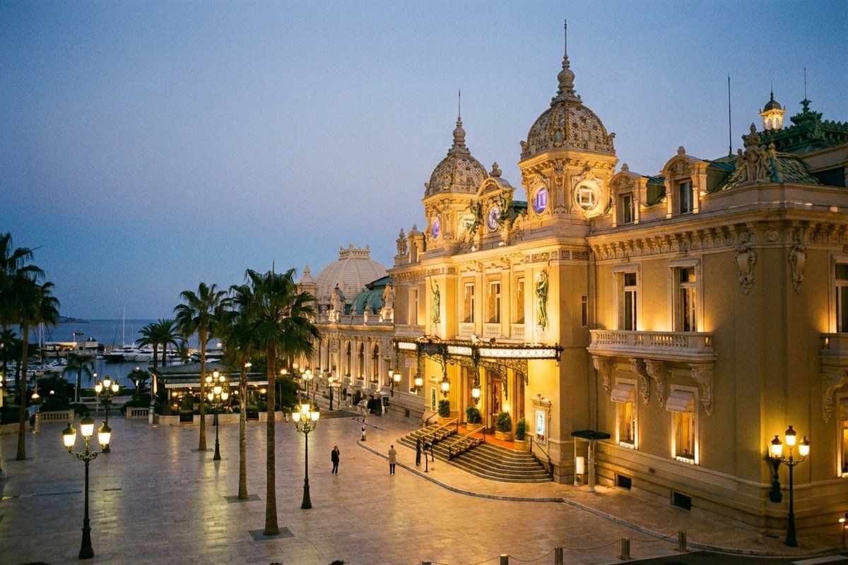 The golden-lit Belle Époque facade of the Opéra Garnier Monte-Carlo at dusk, overlooking the Monaco harbour